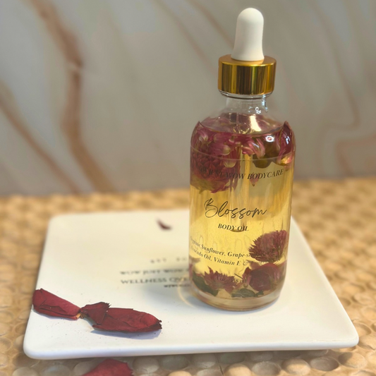 Bottle of 'Blossom' body oil on a white plate with dried flowers. Organic Body Oil (Blossom): Madison Ave Bond #9 Blossom scented body oil for soft, nourished, and nut-free skincare.
