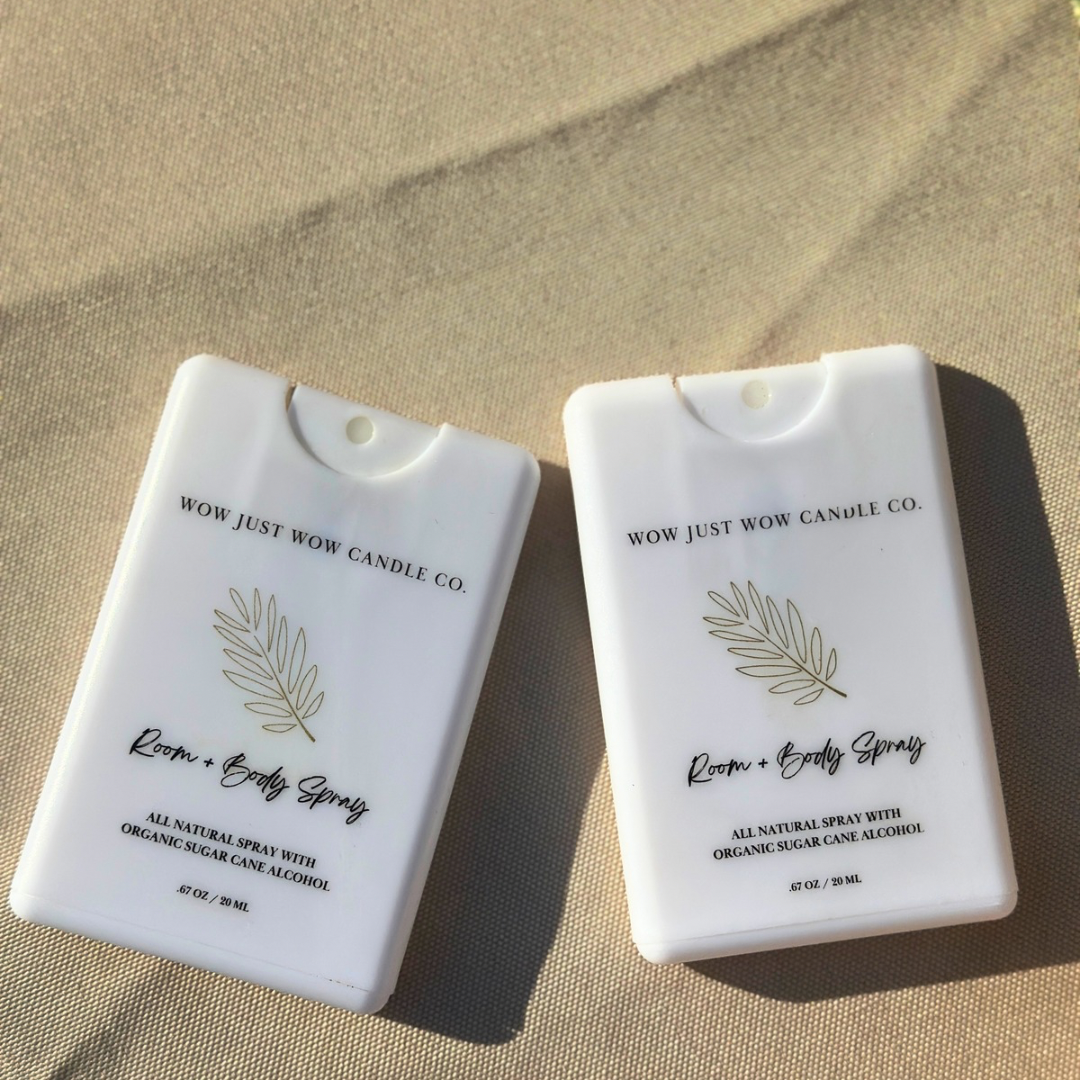 Two white room and body spray containers with leaf design on a beige surface