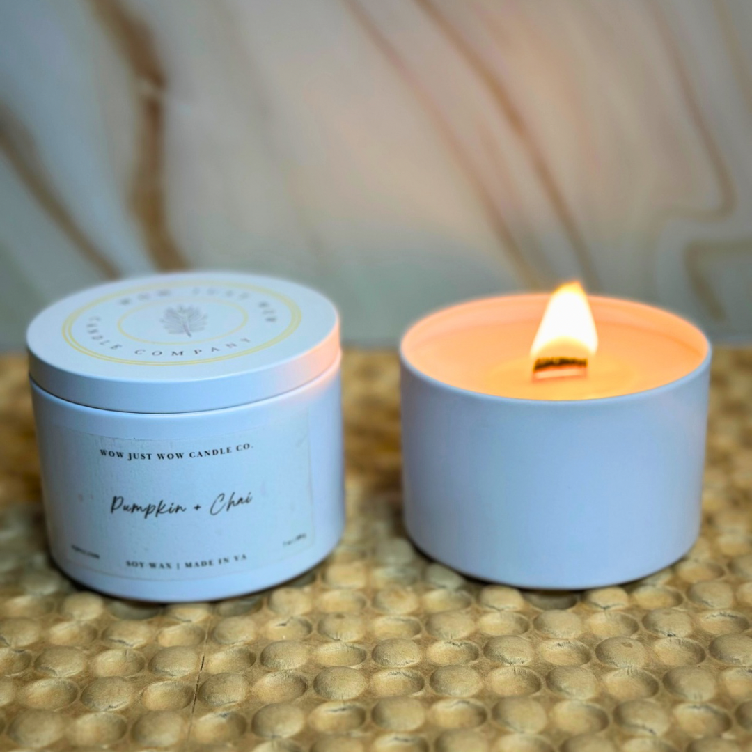Blue soy candle tin labeled Pumpkin + Chai, with lit flame beside matching jar.