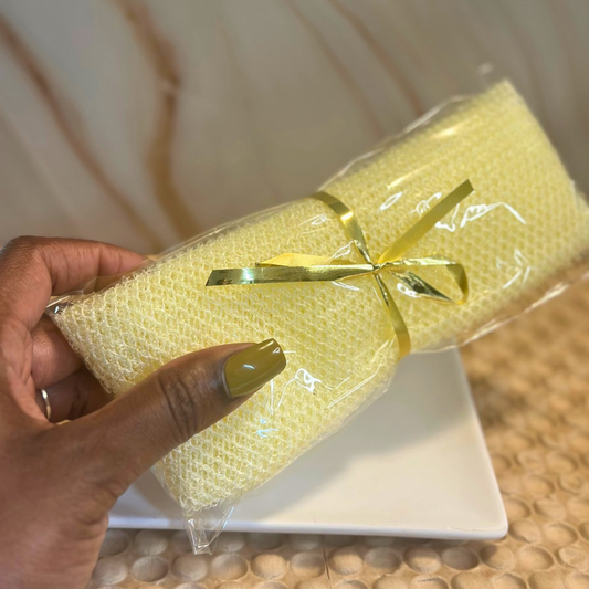 Hand holding a wrapped yellow AFRICAN EXFOLIATING WASH NET with a gold ribbon on a white surface.