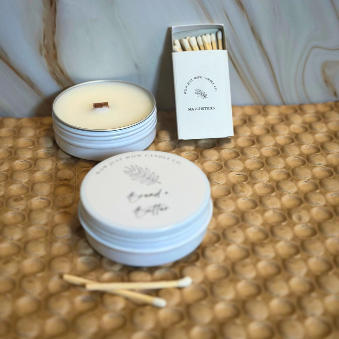White soy candle tin with lit wick and matching lid, plus small matchbook and matches