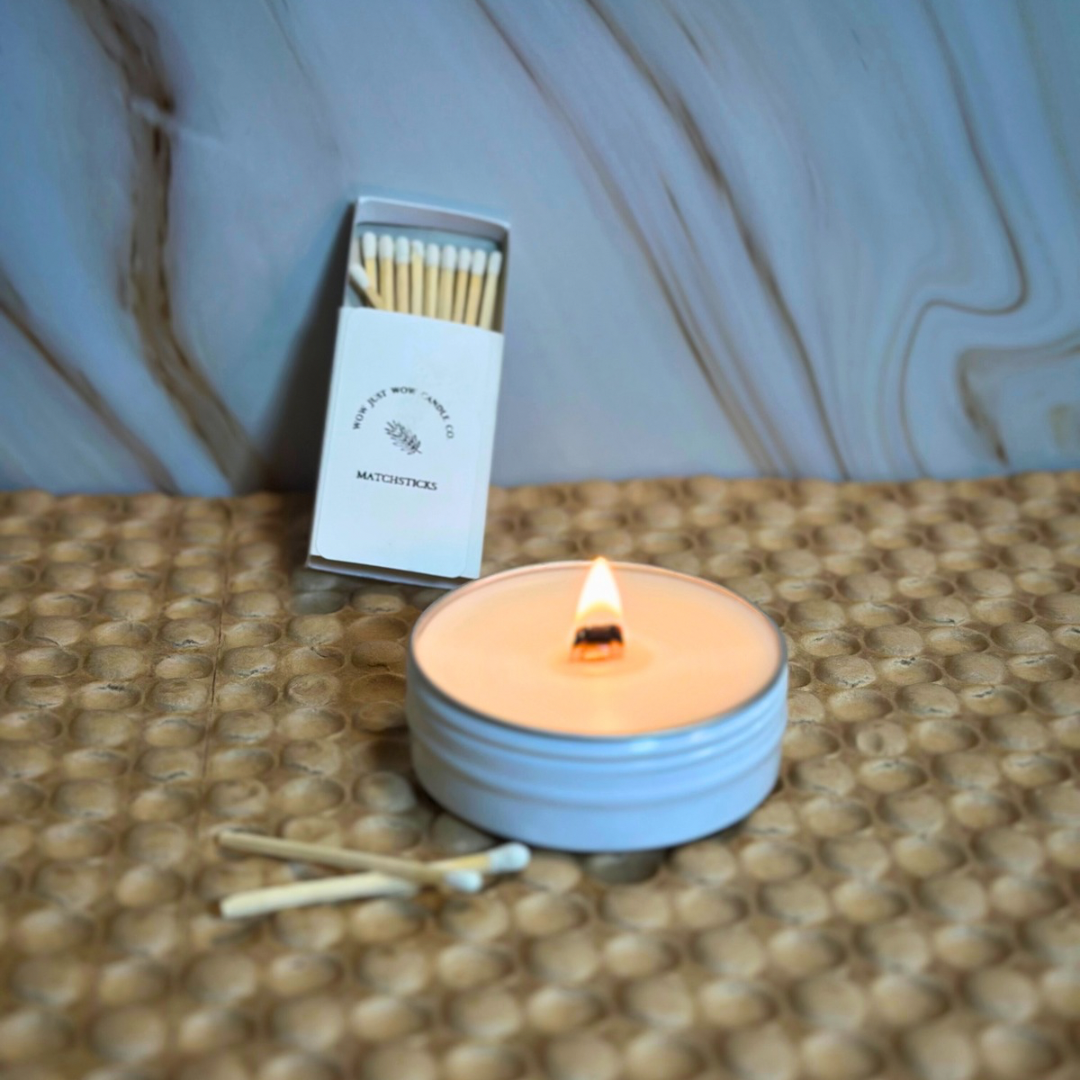 Light blue soy candle with steady flame beside wooden matchbox and matches on textured mat