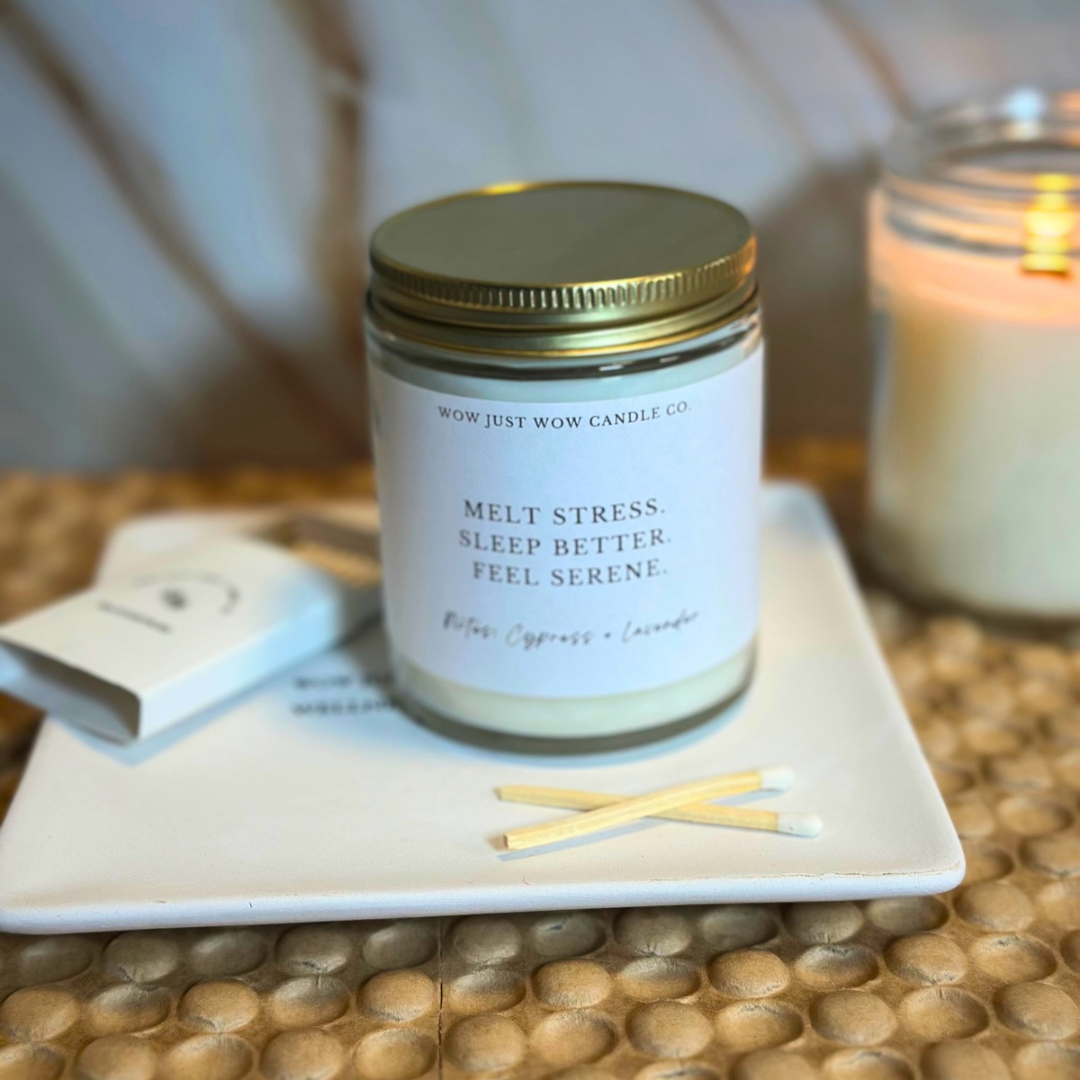 Candle jar labeled 'Melt Stress, Sleep Better, Feel Serene' on a textured surface with matches.