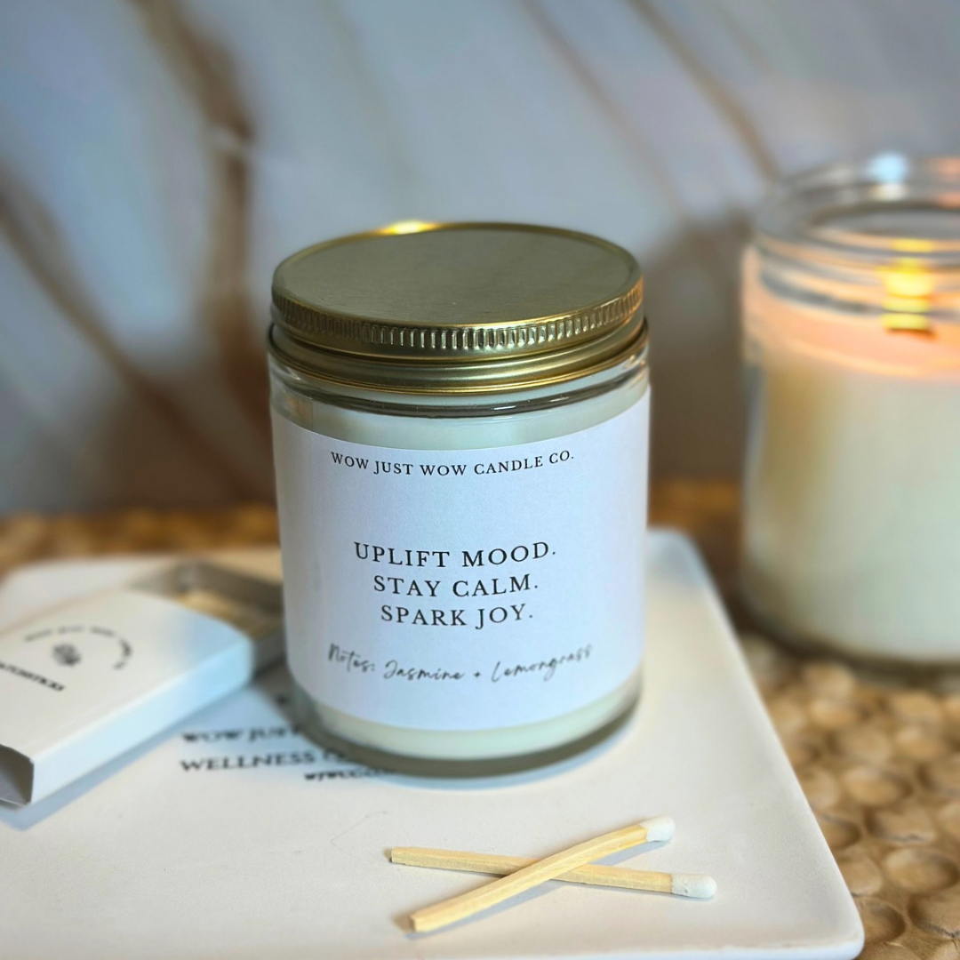 Candle jar with a gold lid on a white coaster with matches, surrounded by soft lighting.