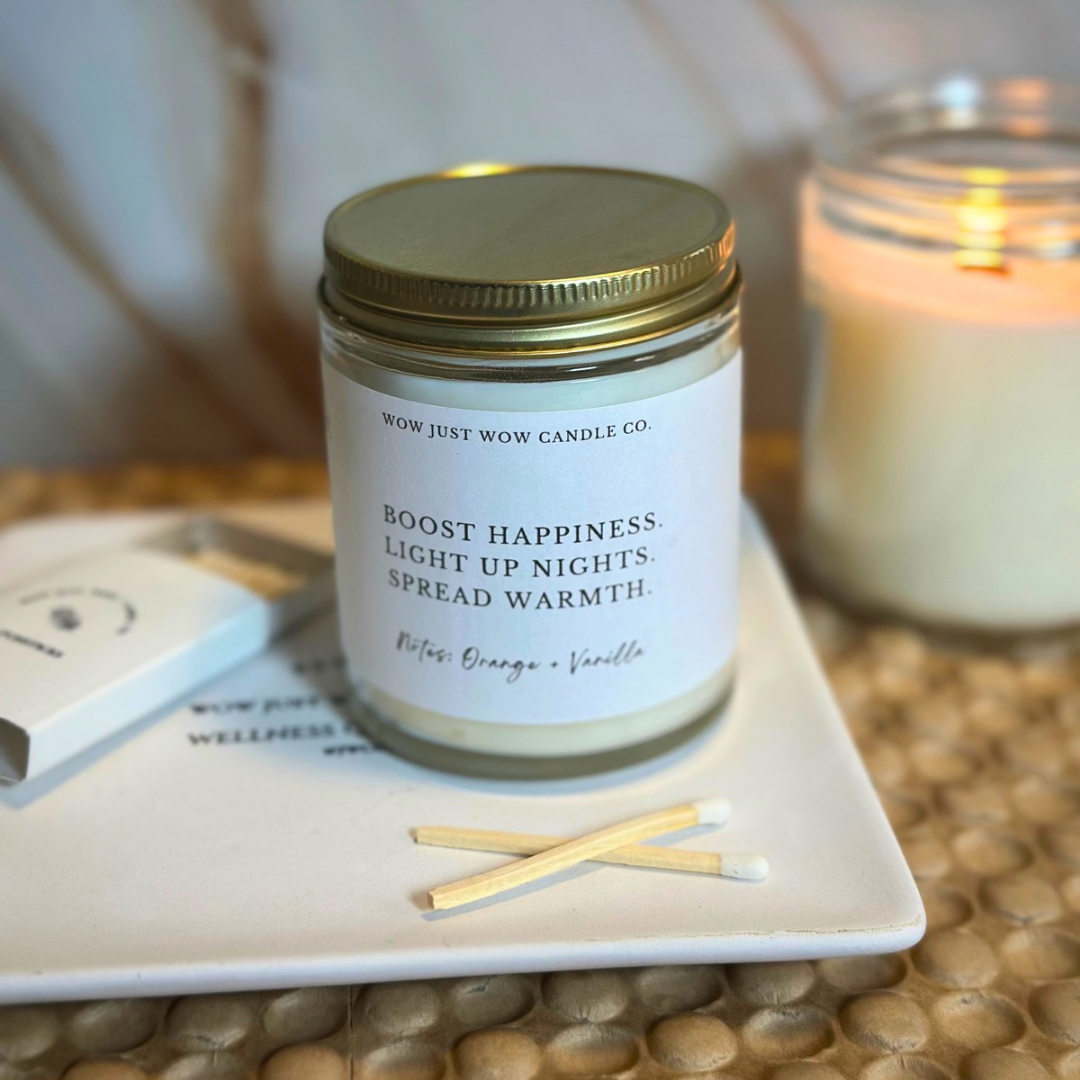 ORANGE AND VANILLA Candle jar with a label on a coaster with matches, on a textured surface.