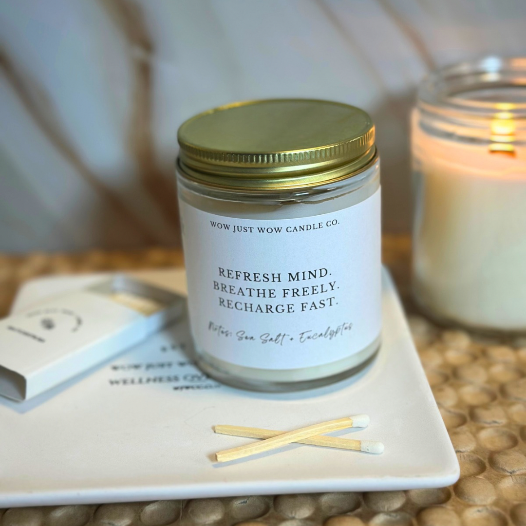 Candle jar with a gold lid on a coaster with matches, surrounded by candles and books.