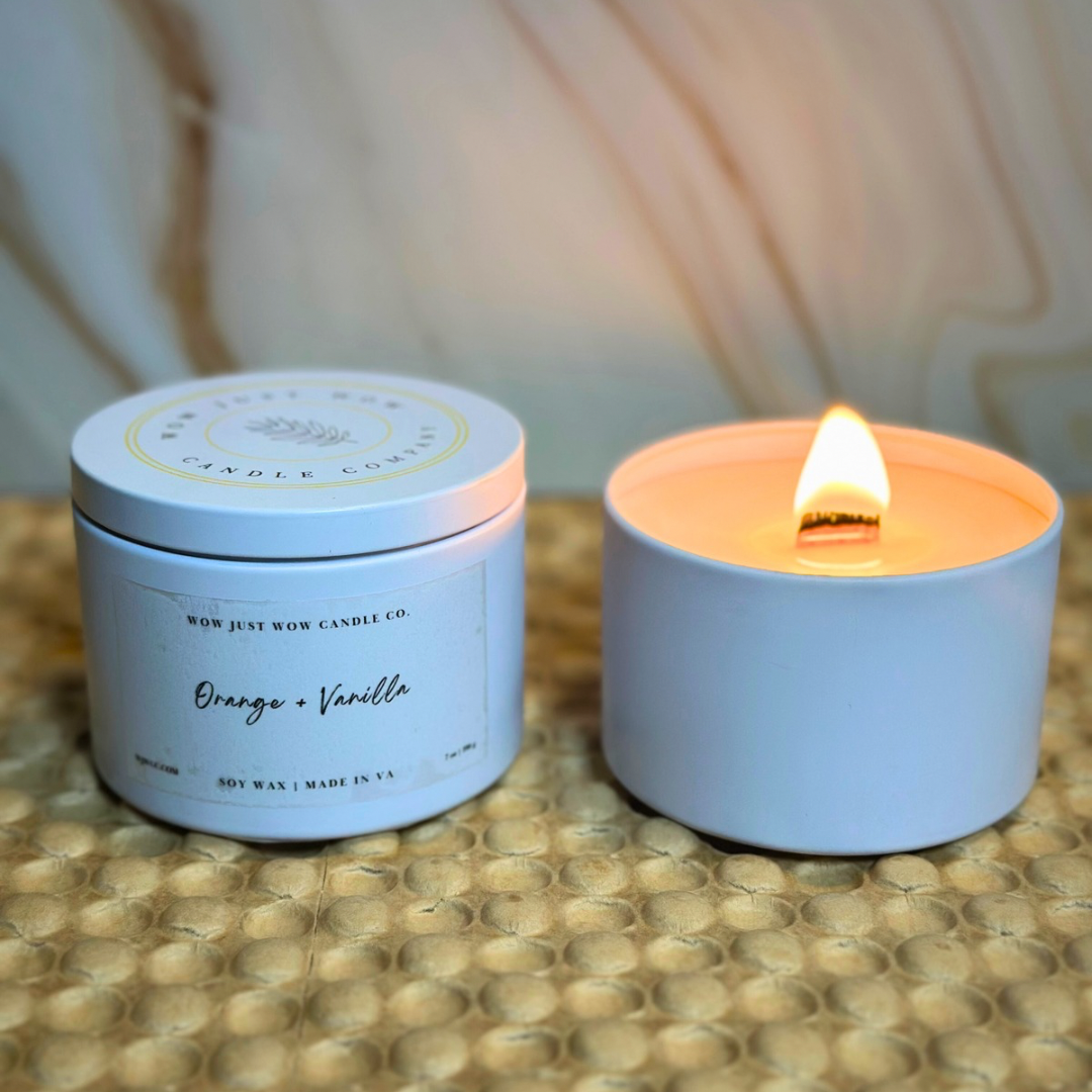 Light blue soy candle in a round tin with orange and vanilla label; flame burning