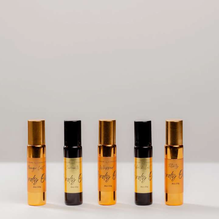 A series of five roll-on body oil bottles with gold caps and clear amber liquid visible inside, labeled with different scent names.