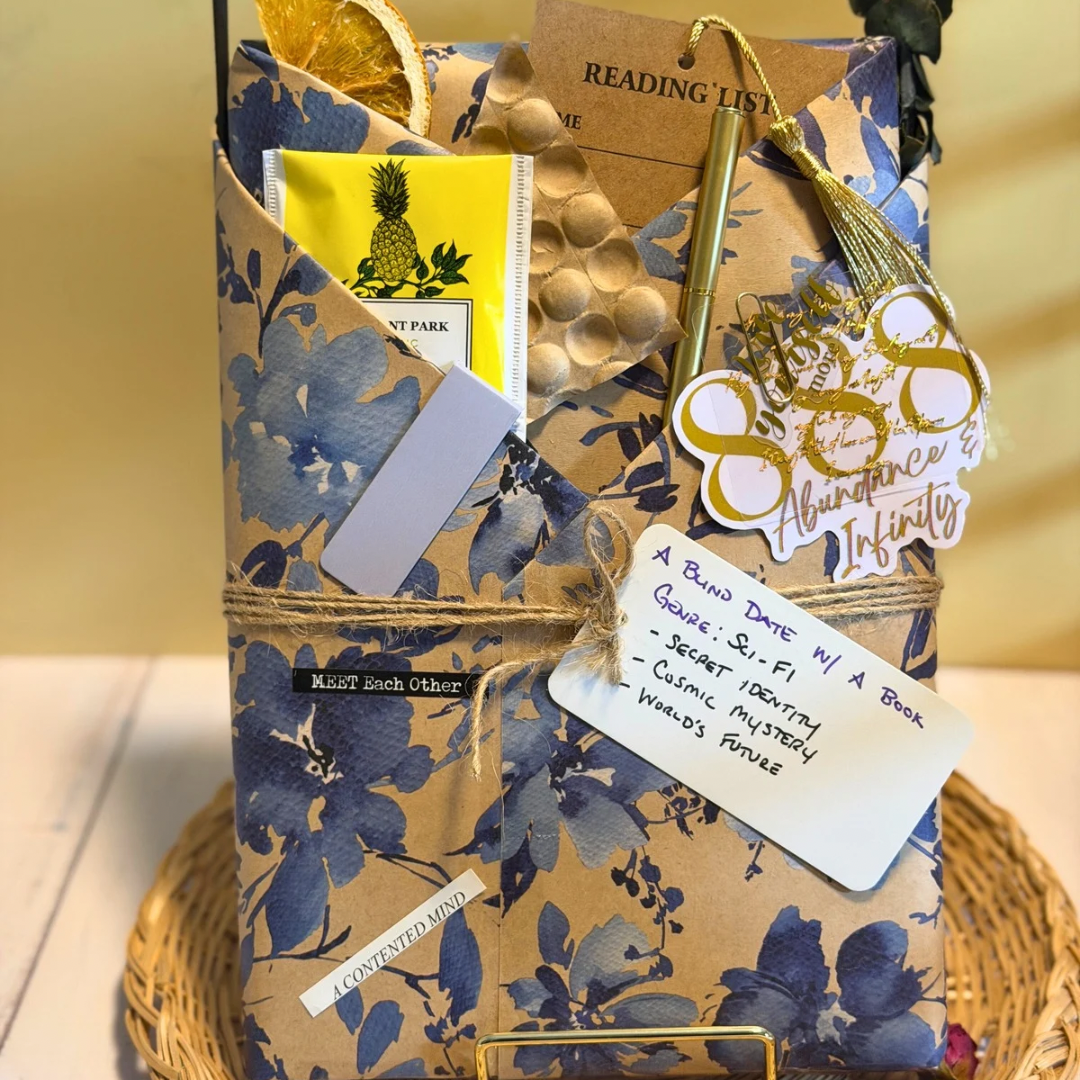 Floral-patterned gift bag with books, a pineapple TEA, and decorative elements on a wooden surface.