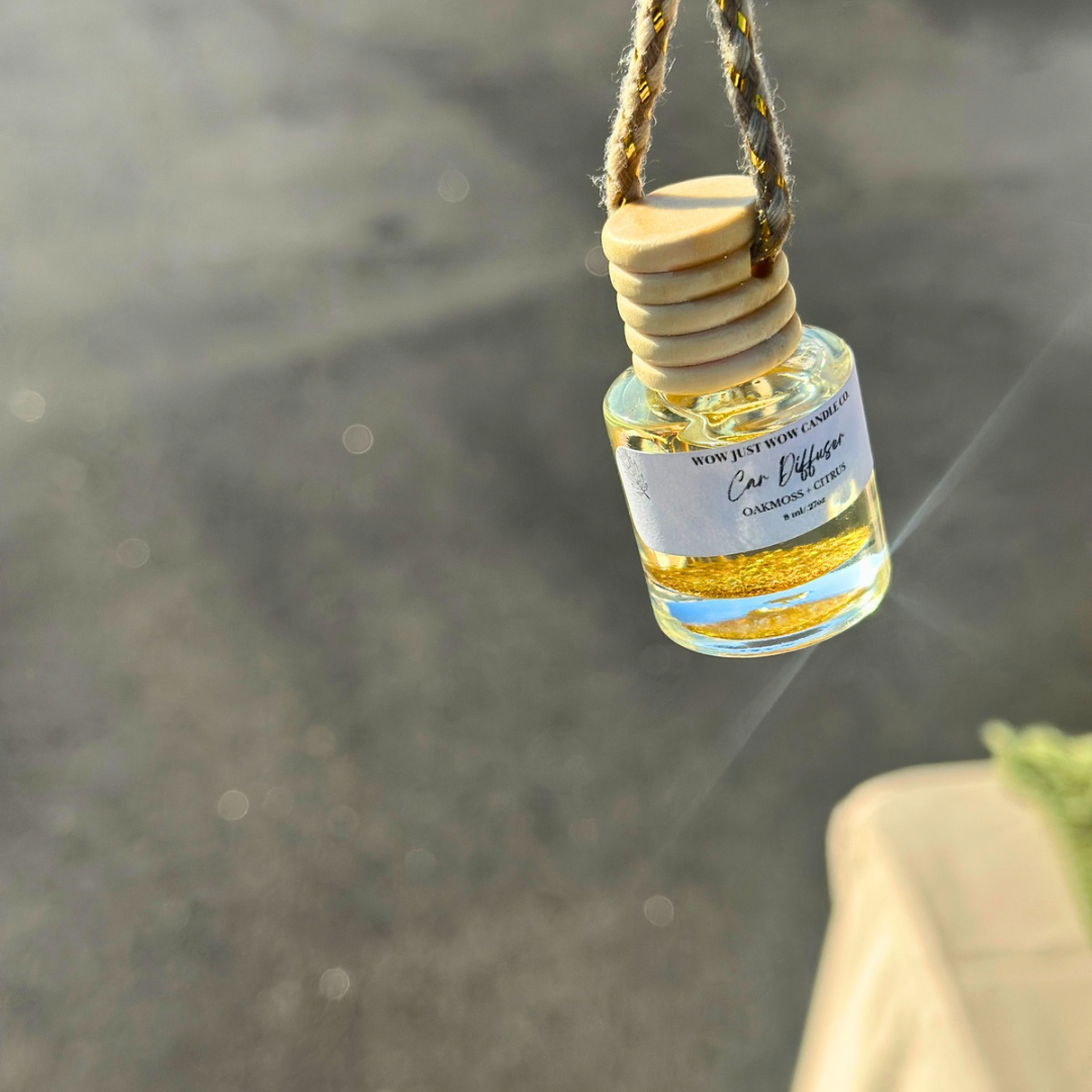 Small bottle CAR DIFFUSER  with GOLD GLITTER AND A wooden cap hanging by a string against a blurred natural background