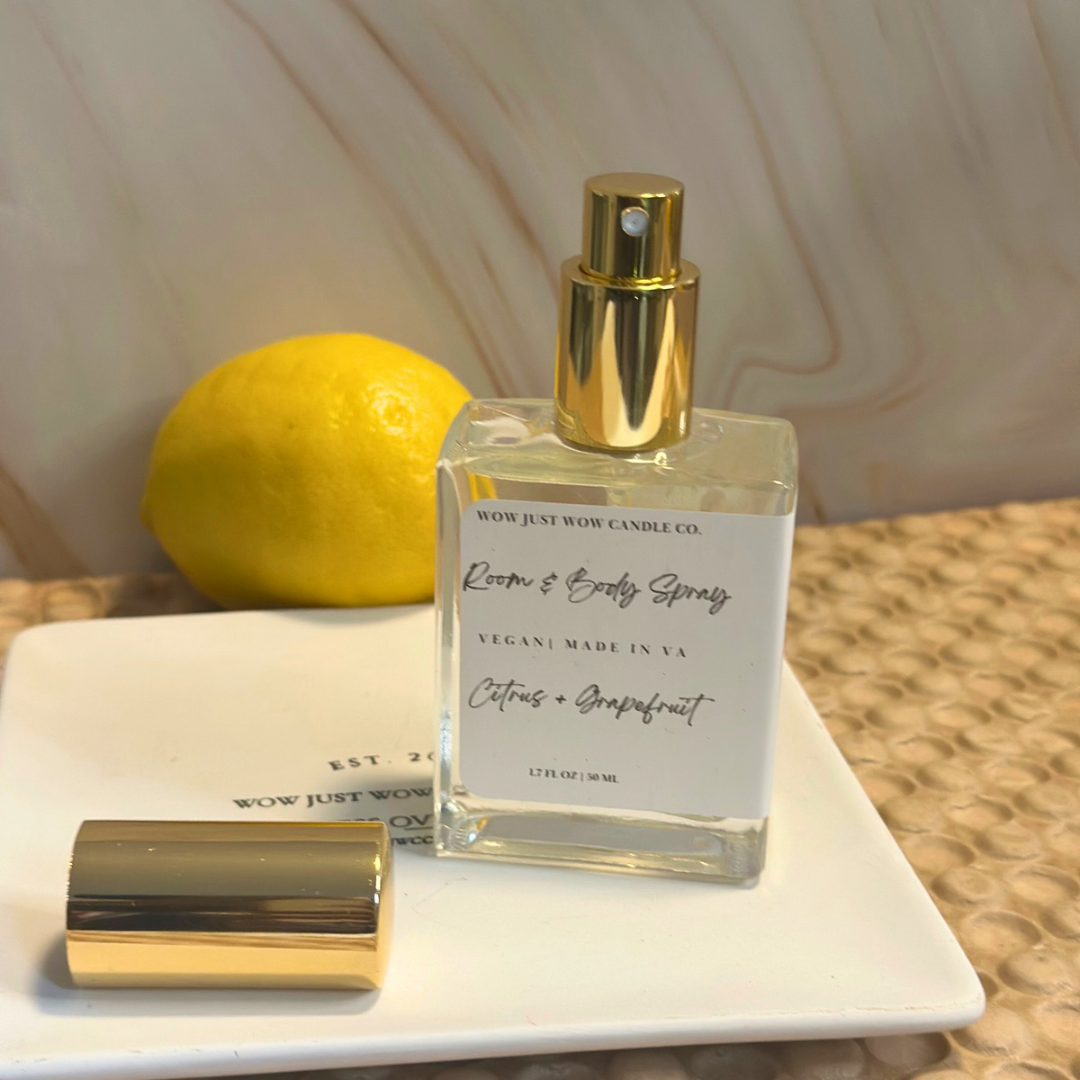 Room and body spray bottle with gold cap on a white surface next to a lemon